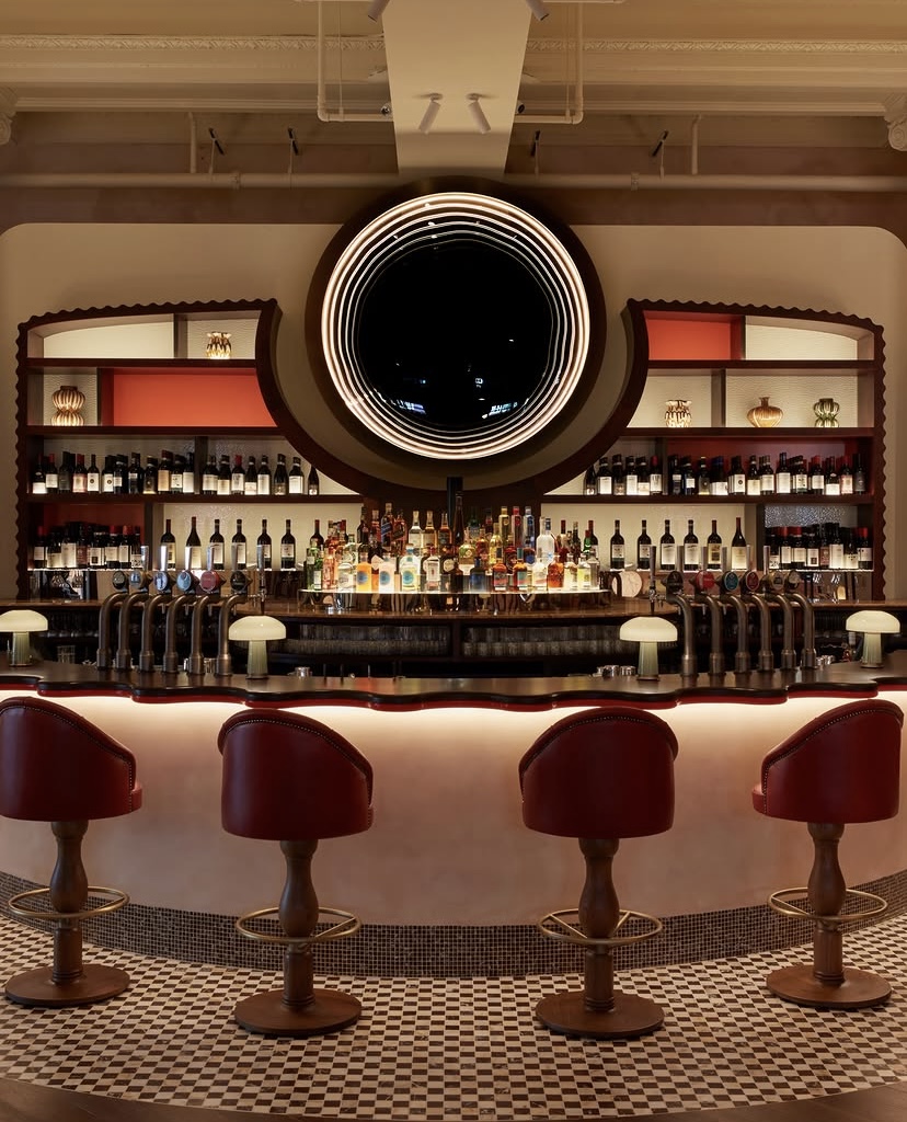 Elegant bar interior at Juno Restaurant in Kensington Olympia, London, featuring red bar stools and illuminated drinks display